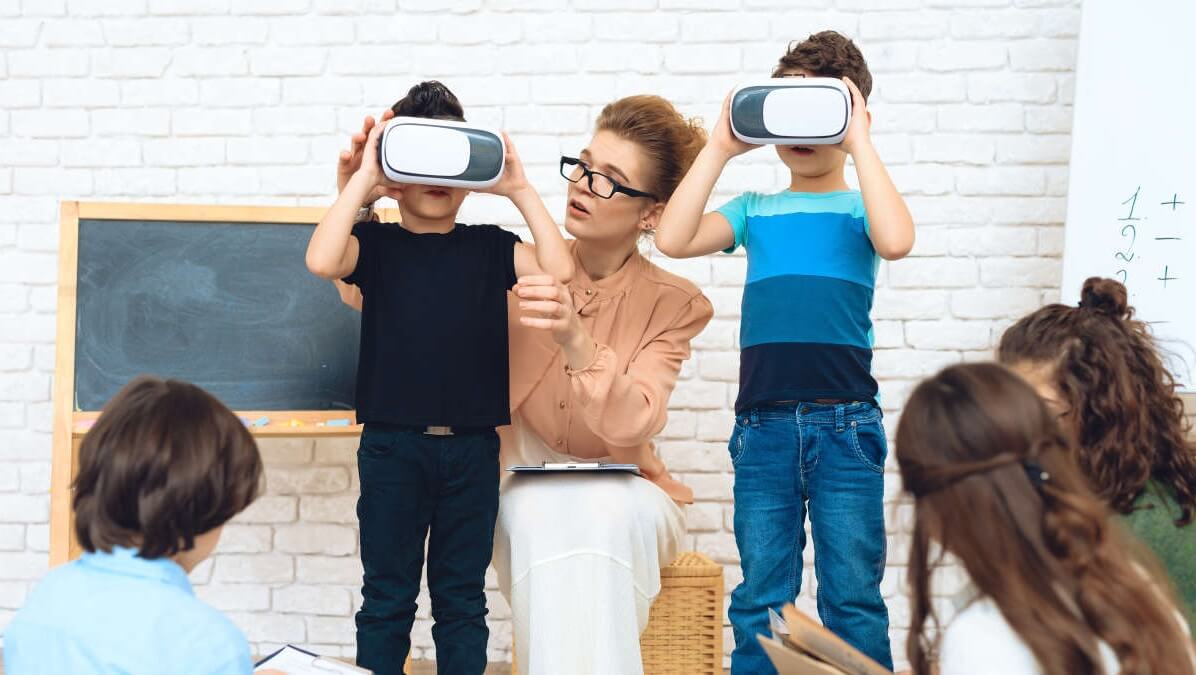 Niños en clase, con gafas de RV, ayudados por la docente